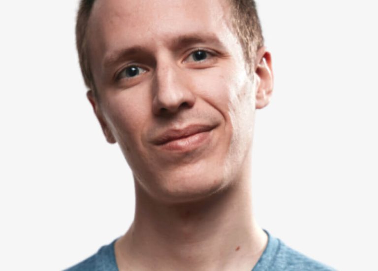 A young adult with short light brown hair and blue eyes, wearing a light blue shirt, facing the camera and smiling slightly against a plain white background.